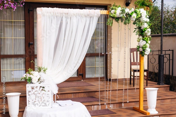 Fototapeta beautiful arc is decorated with white tulle, flowers and chains of transparent beads. A table with a gift box on the background of the restaurant