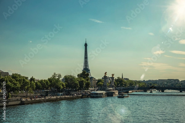 Fototapeta Seine River bank with trees, bridge and Eiffel Tower at sunset in Paris. Known as the “City of Light”, is one of the most impressive world’s cultural center. Northern France. Retouched photo