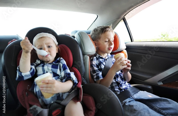 Obraz Little sister and her brother in safety car seat eating sweet ice cream. The little girl is capricious
