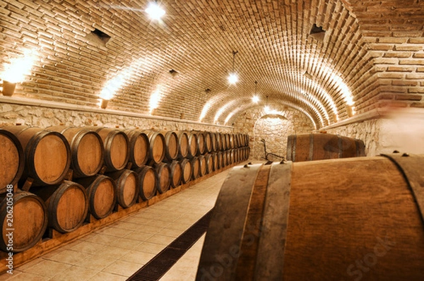 Obraz Wine barrels in the old basement of a winery storage. Cellar of restaurant wine vault with brick stone walls.