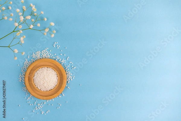 Fototapeta Flat lay Combined bowl with tablets and flower. Homoeopathy  medical grains on a wooden plate, scattered on a table, and a green flowering branch of grass