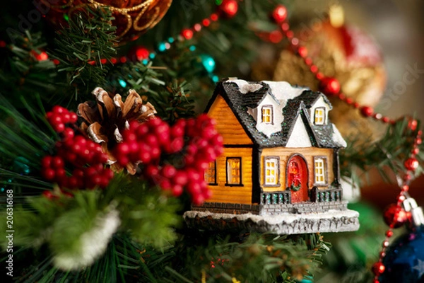 Fototapeta Сказочный дом на новый год. Игрушечный дом на еловых ветках создает сказочный вид. Красочные бусы и игрушки на еловых ветках в новогоднюю ночь.
