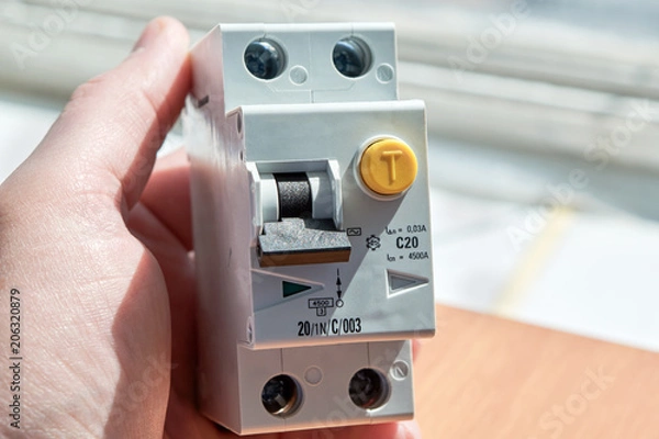 Fototapeta Man holding an automatic switch of differential current. The device protects human life from electric shock. It combines an automatic switch plus a protective shutdown device.