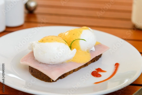 Fototapeta Egg benedict on white dish on breakfast - Poached egg on ham slices and a piece of bread