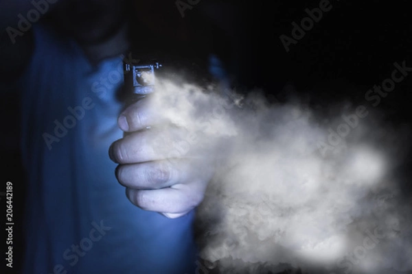 Obraz a man's hand holds a gas pepper spray in the dark, a black background. concept of safety and self-defense