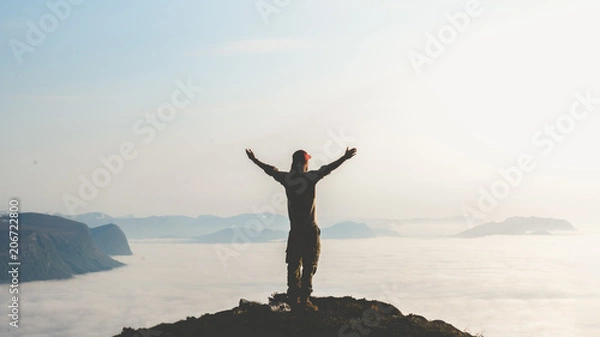 Fototapeta Young man stand on top of mountain top with hands raised in the air. Success and risk concept.
