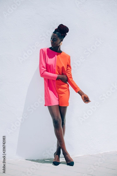 Obraz Exotic portrait of a beautiful and attractive black model woman wearing a red and pink dress with a fashion makeup posing on white background. Exotic fashion concept