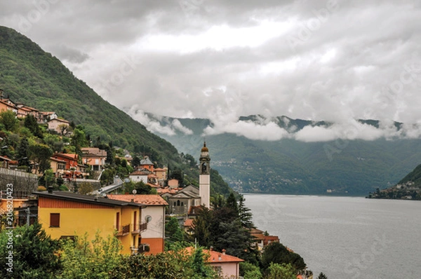 Fototapeta Overview of Lake Como shore with mountains and villages in a cloudy rainy day. Near the city of Como, a pleasant town a few miles from Milan. Located in the Lombardy region, northern Italy