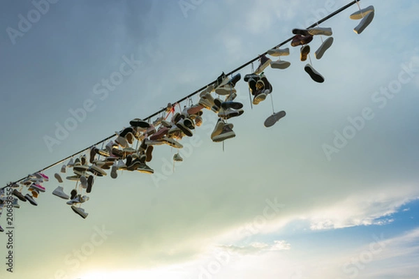 Fototapeta a lot of pairs of shoes hung on a rope for tied shoelaces, against a cloudy sky