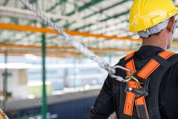 Fototapeta Construction worker wearing safety harness and safety line working on construction