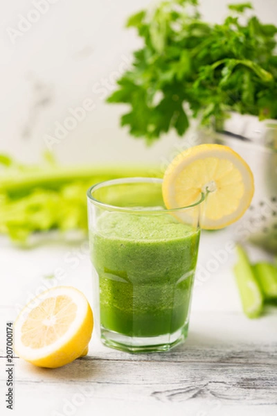 Fototapeta Green cocktail smoothie parsley celery lemon lime slices, healthy drink ingredients, glass of beverage on white wooden table, detox diet clean eating, with vegetables on table