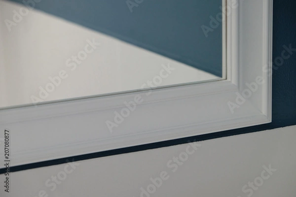 Obraz Corner of mirror with white frame in perspective view and reflection of navy blue color wall in the bathroom