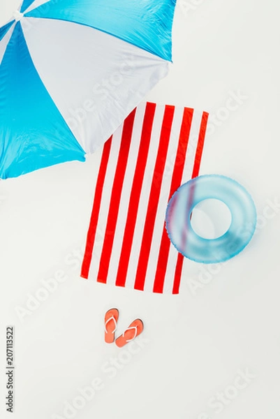 Fototapeta top view of beach umbrella, striped beach towel, flip flops and inflatable ring isolated on white