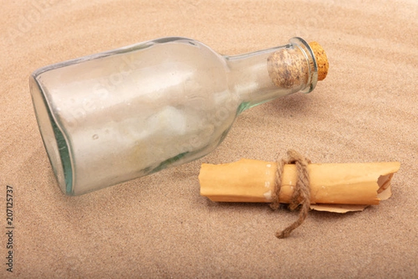 Fototapeta Wrapped message beside an old bottle on the sand of a beach