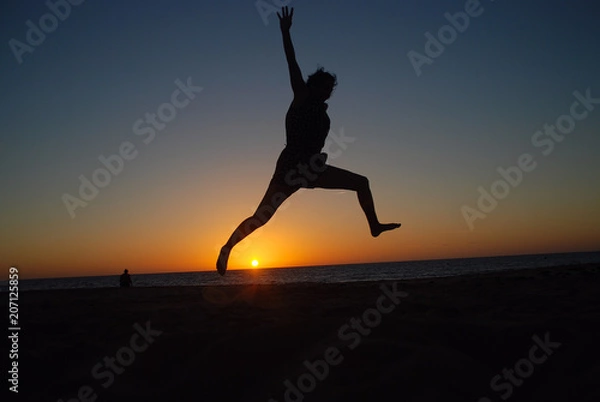 Obraz CHICA SALTANDO EN LA PLAYA AL ATARDECER