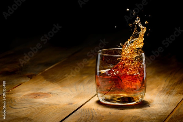 Fototapeta Whisky splash w szkle na drewnianym stole.