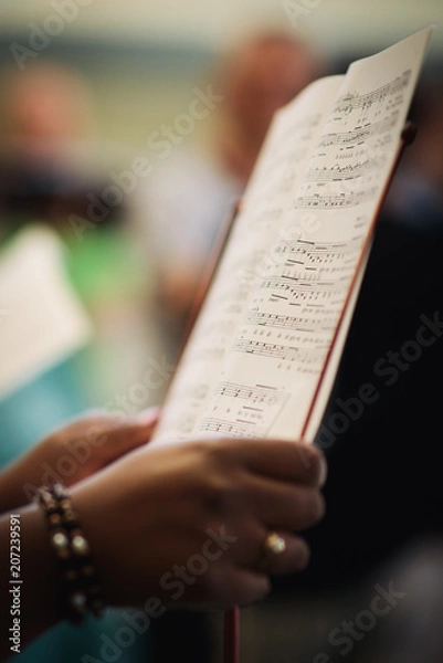 Fototapeta A woman sings in a choir and holds her sheet music notes