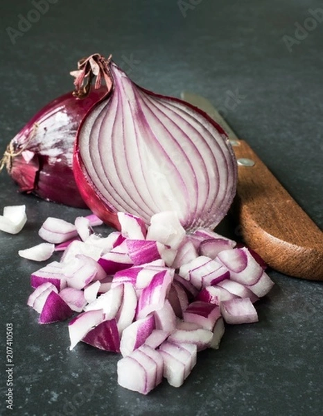 Fototapeta Chopped up red onions with knife on a dark stone surface