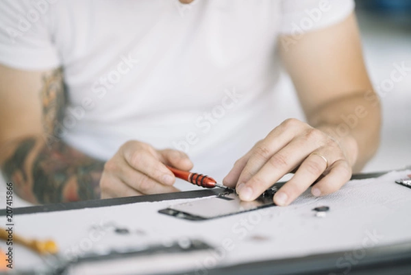 Fototapeta Electronics repair service. Technician disassembling smartphone for inspecting.