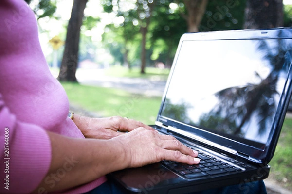 Fototapeta The elderly use a notebook computer to communicate in the garden.