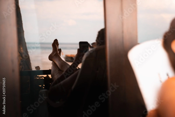 Fototapeta young female tourist relaxing on the beach while internet surfing with smartphone