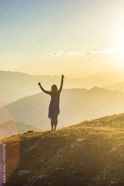 Obraz girl in dress with hands up standing on grass in sunset mountains