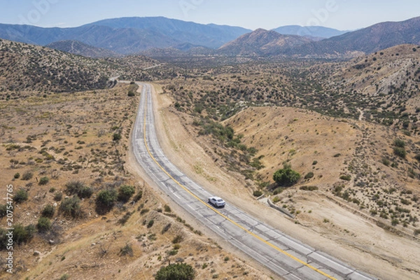 Fototapeta Single car on empty wilderness road in the Mojave Desert of southern California.