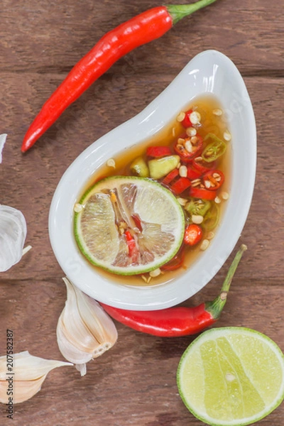 Fototapeta Fish sauce with slice lime and red hot chili in white bowl on wooden table, Thai food