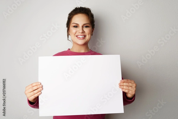 Fototapeta Beautiful smiling young women with banner sign with white blank empty paper billboard with copy space for text over gray background