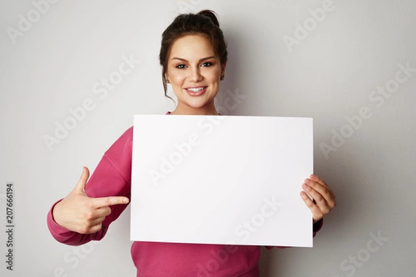 Fototapeta Pretty smiling woman holding empty blank board isolated on the gray background