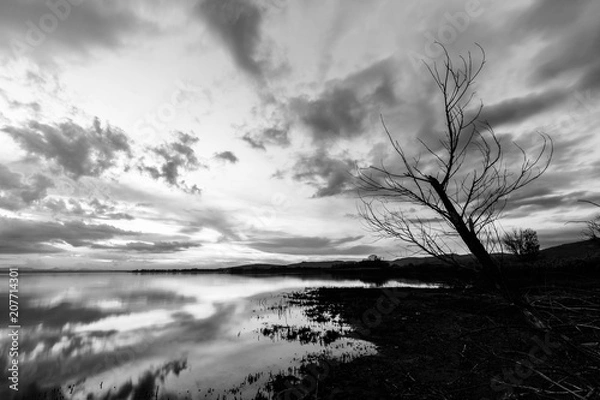 Fototapeta Lake shore at sunset, with perfect reflections of some clouds on