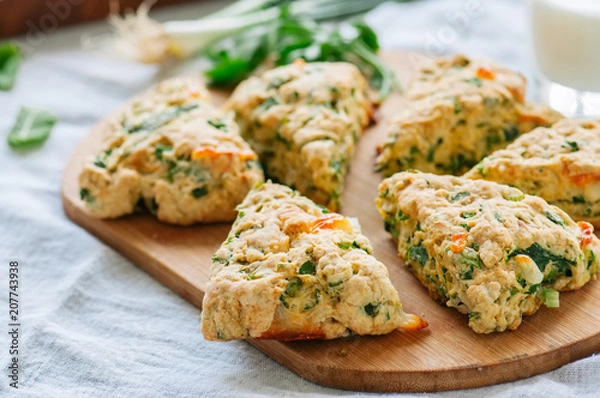Fototapeta Savory scones with feta and mozarella and green herbs on a wooden board.