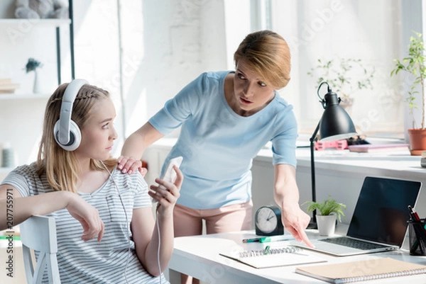 Obraz mother forcing her daughter to do homework while she listening music with headphones