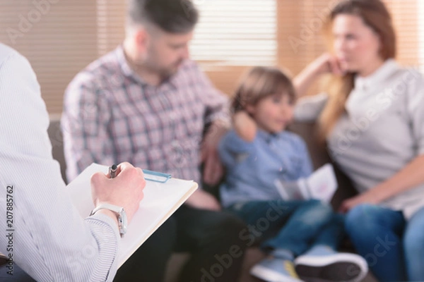Obraz Ręka profesjonalnego psychoterapeuty rodzinnego pisania notatek przed parą z dzieckiem na niewyraźnym tle podczas konsultacji