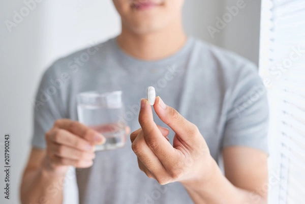 Obraz Happy asian man holding a pill and a glass of water looking at camera