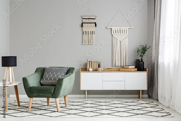 Fototapeta Green armchair on patterned carpet near table with lamp in minimal living room interior. Real photo
