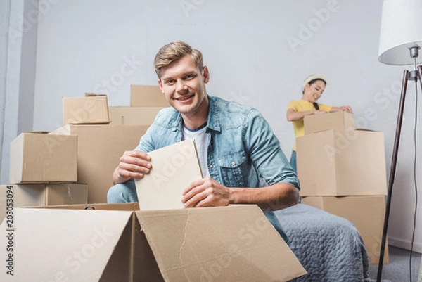 Fototapeta beautiful young couple unpacking boxes while moving into new home