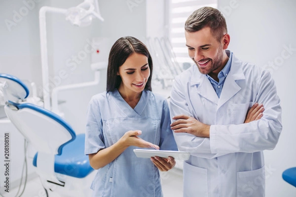 Fototapeta dentist and assistant looking at digital tablet screen