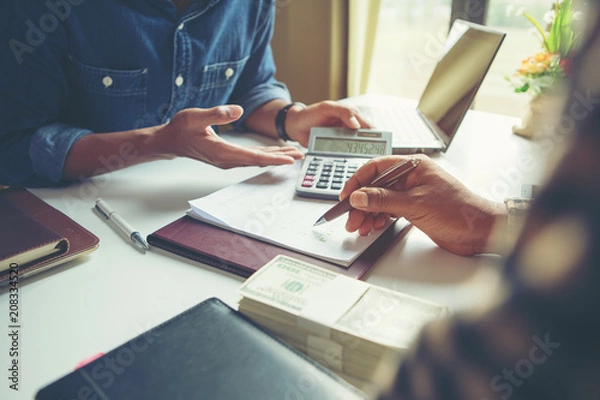 Fototapeta Calculate budget and business planning concept, two people couting revenue and expenditure by using calculator and looking paper graph on desk in home office