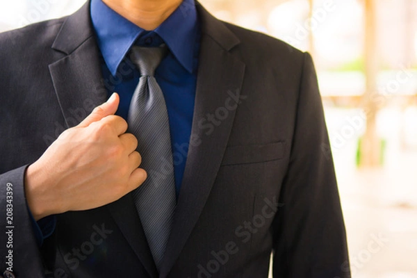 Fototapeta Asian business man is touching one side of his black formal suit for talent concept in working.