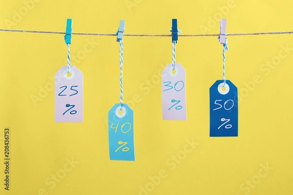 Fototapeta On a yellow background photographed labels. Four colorful empty labels hang on a rope pinned with clothespins. Each label has a discount of twenty-five, thirty, fifty percent. Bright layout mock up.
