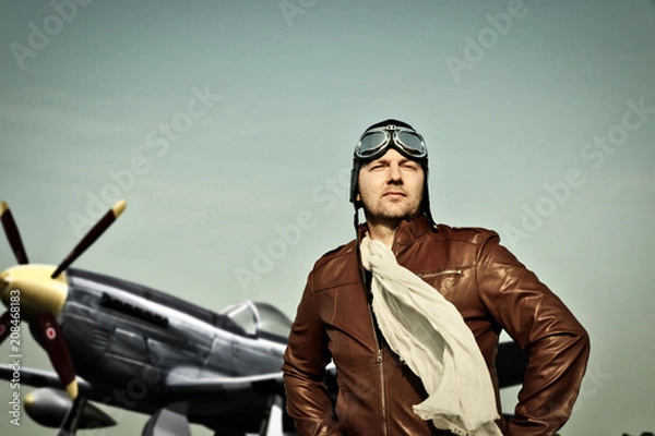 Obraz Portrait of a vintage pilot with leather cap, scarf and aviator glasses in front of a historic airplane - Portrait of a man in historical pilot clothing