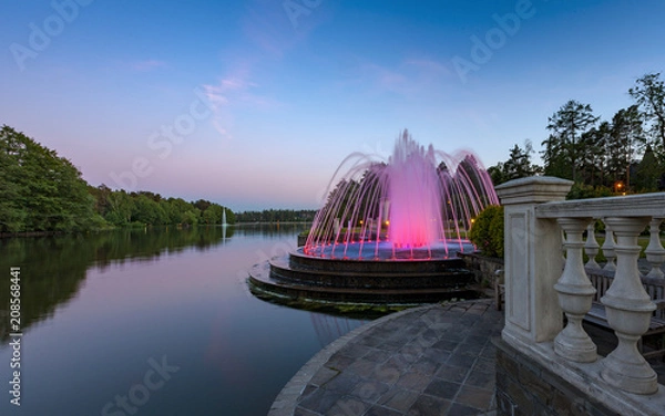 Fototapeta Fountain with illumination on the shore of the evening lake