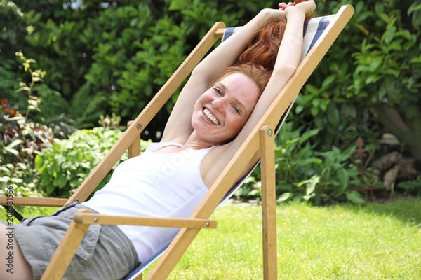 Fototapeta Hübsche rotharrige Frau sitzt lachend in einem Liegestuhl