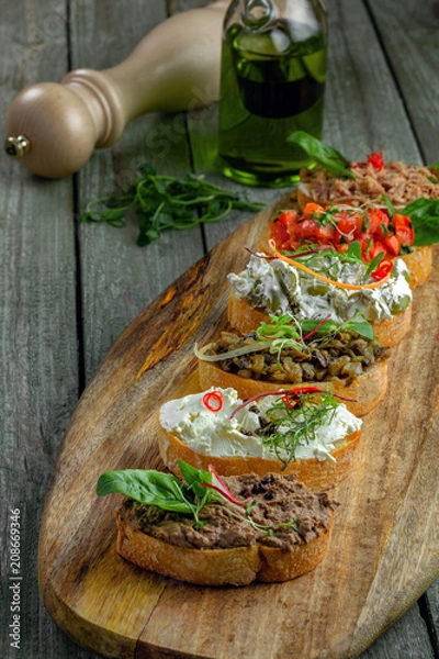 Obraz Antipasto bruschetta set made of toasted bread with tomato, meat pate, olives, cream cheese and tuna salad. Classic Italian appetizers on a rustic table.