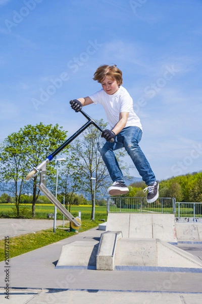 Fototapeta boy has fun jumping with the push scooter at the skate park