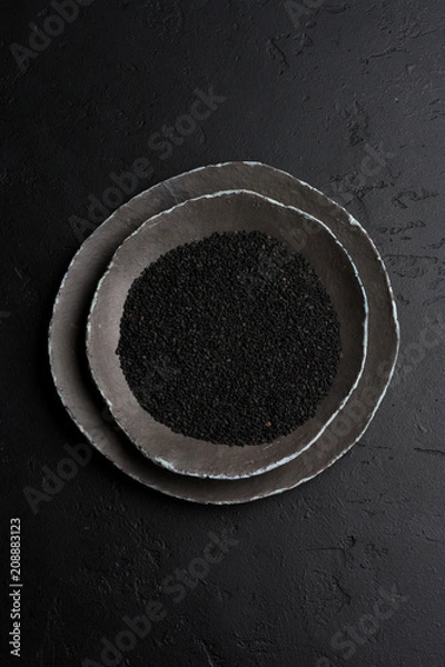 Obraz Czarne nasiona sezamu w czarnych ceramicznych płytach na ciemnym starym tle vintage. Rustykalny styl. Widok z góry.