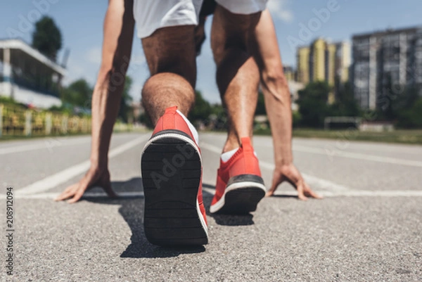Fototapeta back view of male sprinter in starting position on running track