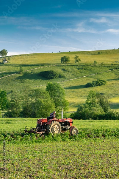 Obraz Farmer on a tractor working in a field, in a small, charming village located in low Pieniny in Poland