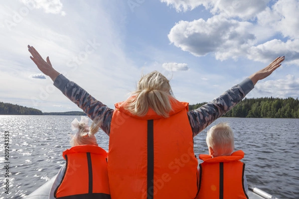 Fototapeta Girl in a life jacket floating on the boat with his hands up. Children in life jackets sitting next